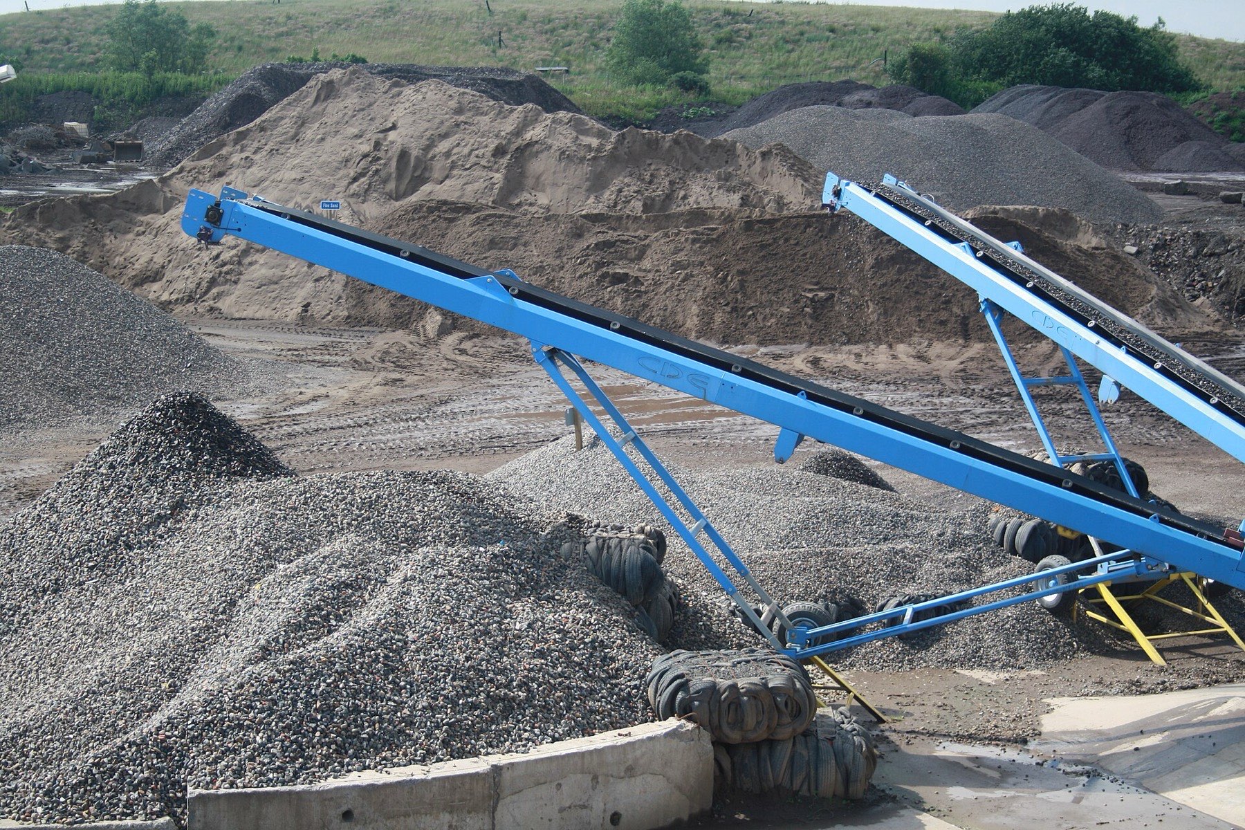 Grey aggregate heaps under blue stacking conveyors in a quarry yard